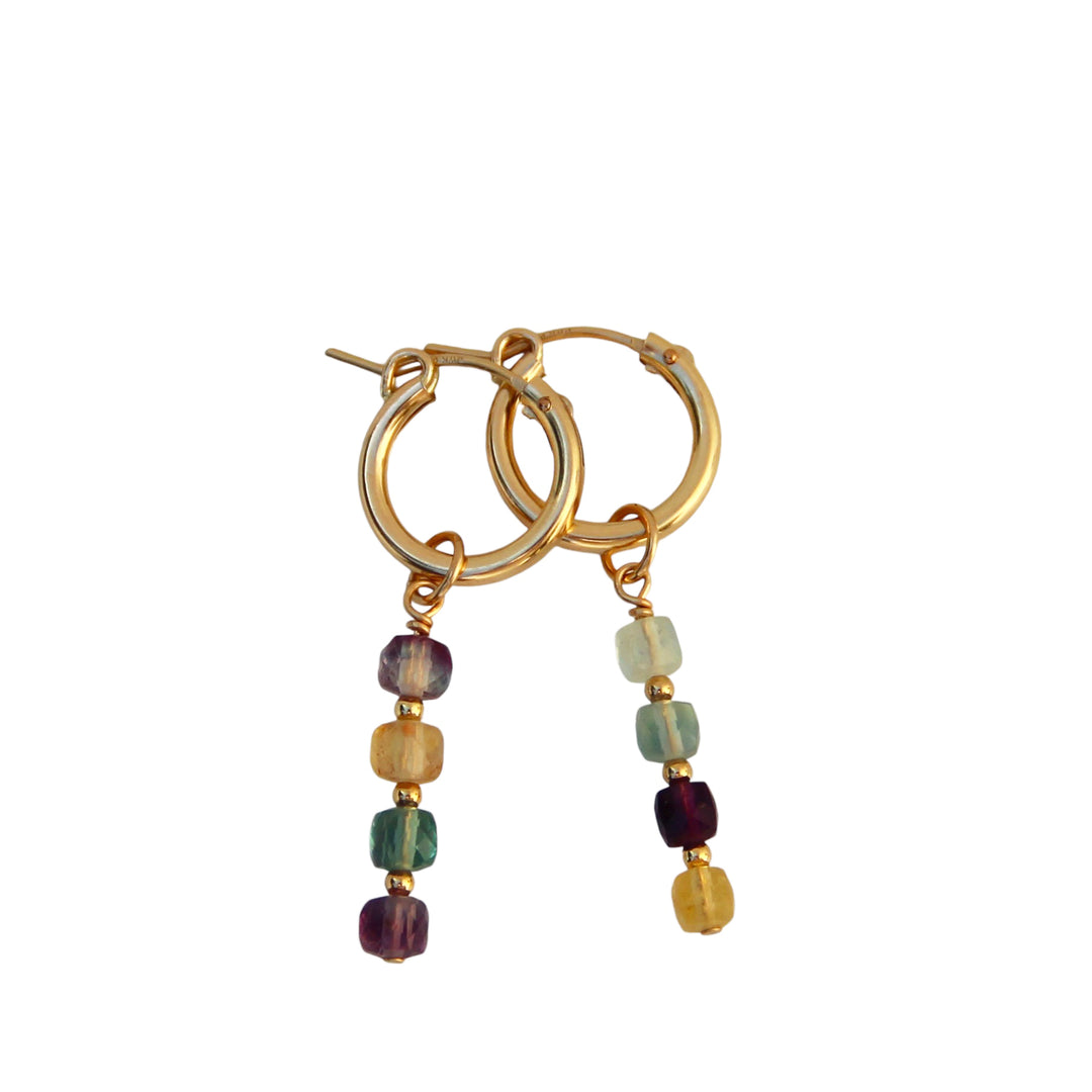 Product image of Aurora Fluorite Gemstone Hoop Earrings by Blooming Lotus Jewelry. These gold hoops feature a delicate cascade of colorful fluorite cube-shaped gemstone beads, each stone offering unique hues of green, purple, and yellow. The natural beauty of the gemstones adds an earthy, bohemian touch to these elegant earrings.