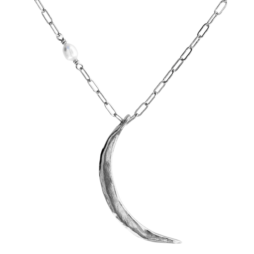 A large skinny crescent moon necklace with an organic texture, handcrafted in silver with a delicate pearl accent on a paperclip chain.