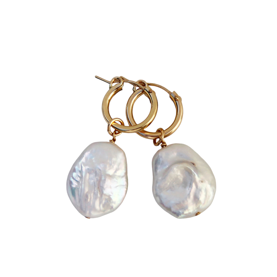 Product image of Ocean Mist Pearl Hoop Earrings by Blooming Lotus Jewelry. These gold hoops feature large, irregular freshwater pearl charms, each with a lustrous, natural finish that evokes the beauty of the ocean. The organic shape of the pearls adds a unique, beach-inspired touch to these sophisticated earrings.