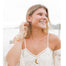 Close-up of woman by the water wearing large gold Olive Branch hoop earrings with a nature-inspired design, paired with a boho lace top, layered necklaces, stacked bracelets, and multiple rings. Her look is effortless and beachy, embodying a peaceful, free-spirited style