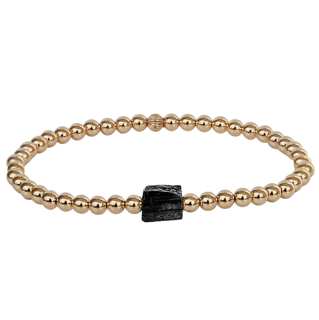 Gold beaded stretch bracelet featuring a raw black tourmaline gemstone at the center, designed for protection and grounding. A minimalist yet powerful accessory with a modern, effortless style.