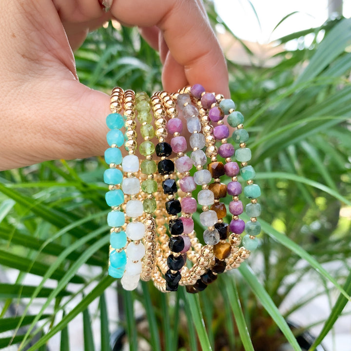 Gold Beaded Bracelets with faceted gemstones held in hand with plants in background - Blooming Lotus Jewelry