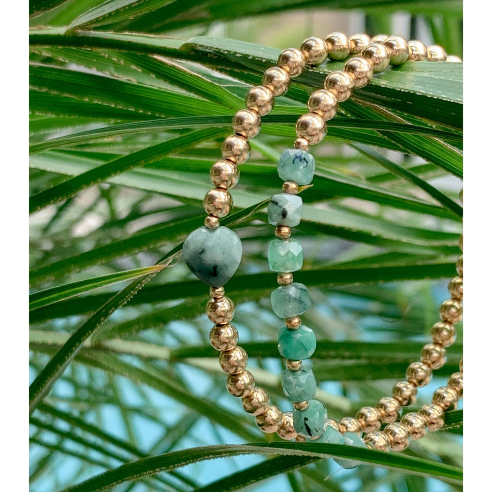 Gold Beaded Bracelets emerald cube gemstones hanging on plant leaves closeup - Blooming Lotus Jewelry