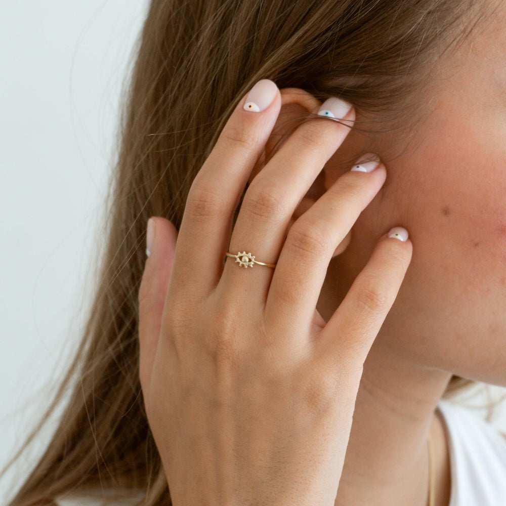 Close-up of a woman wearing the Tiny Eye of Protection Ring in gold on her finger. The delicate eye design with radiant detailing stands out as a symbol of intuition and protection. Her hand, featuring minimalist nail art, gently touches her face, showcasing the ring's elegant and dainty style. Styled by @m.o.n.a.j on Instagram.