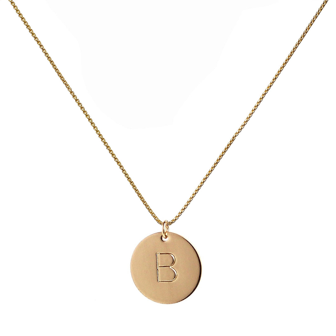 Gold hand-stamped initial disc necklace featuring one personalized pendant on a gold chain, perfect for custom gifts and everyday wear. Handmade by Blooming Lotus Jewelry.