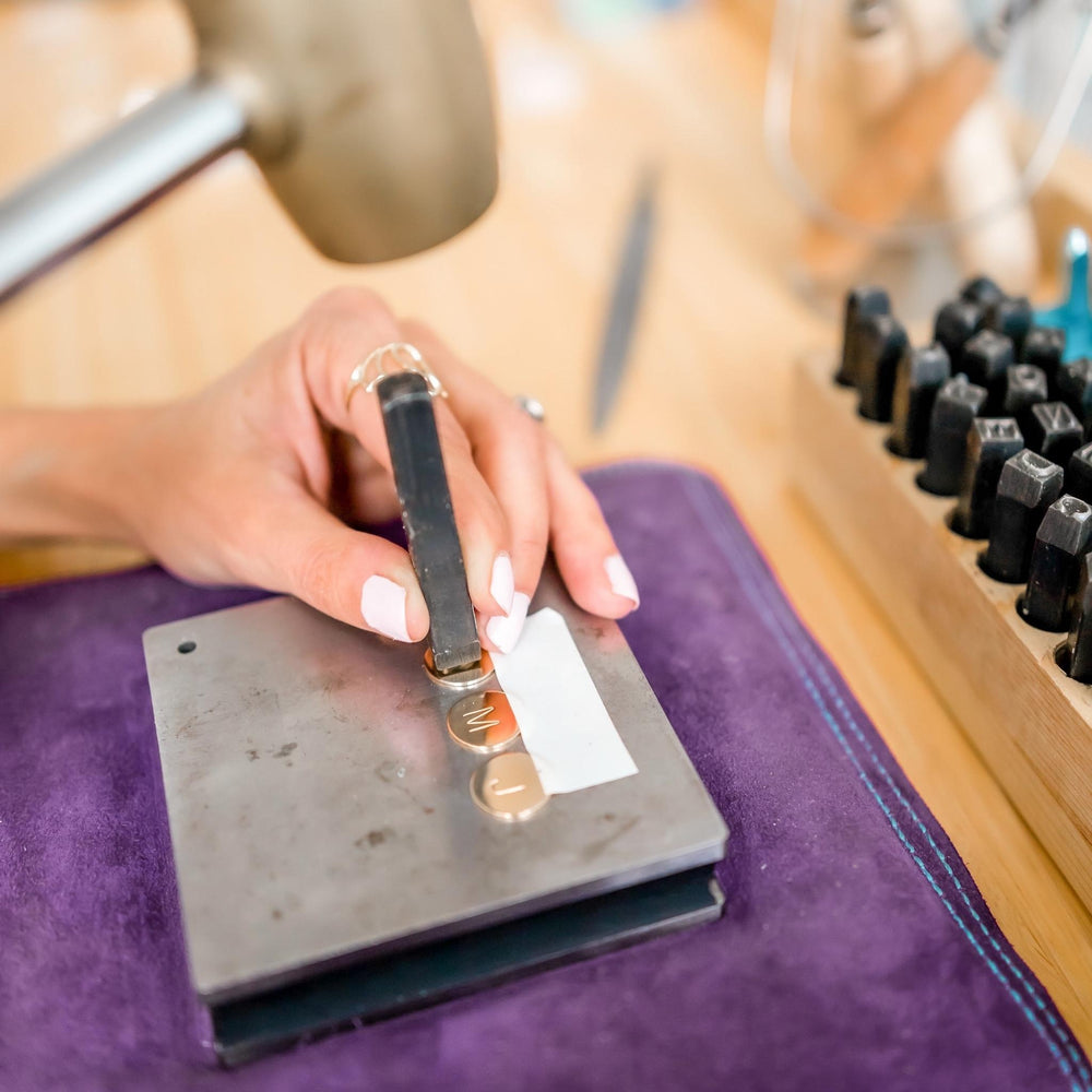 Jewelry designer hand-stamping gold initial pendants using a custom stamping tool, showcasing the craftsmanship behind personalized necklaces from Blooming Lotus Jewelry.