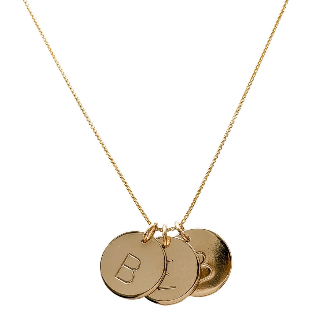 Gold hand-stamped initial disc necklace featuring three personalized pendants on a gold chain, perfect for custom gifts and everyday wear. Handmade by Blooming Lotus Jewelry.