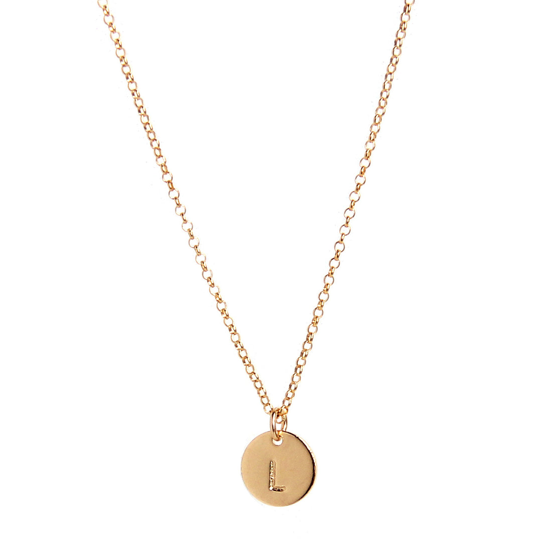 Gold necklace featuring one small round disc pendant, hand-stamped with a single initial 'L,' hanging delicately from a fine chain for a minimalist and personalized style.