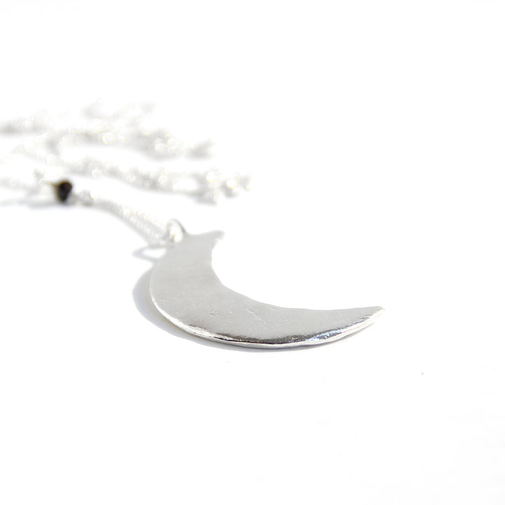 Close-up side view of the Luna Crescent Moon Necklace, featuring a polished silver crescent moon pendant resting on a bright white background, with the delicate silver chain softly blurred in the background.
