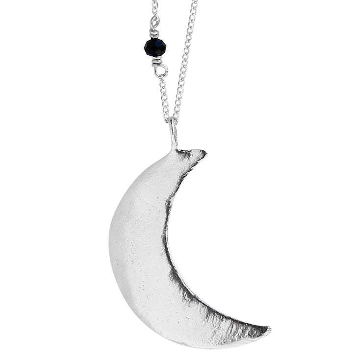 Close-up of the Luna Crescent Moon Necklace featuring a large, textured crescent moon pendant crafted in sterling silver, hanging from a delicate silver chain with a small black faceted spinel gemstone. Displayed against a white background.