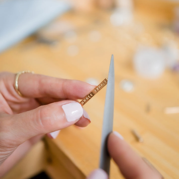 Jeweler's bench filing a mantra bar pendant in hands close up - Blooming Lotus Jewelry