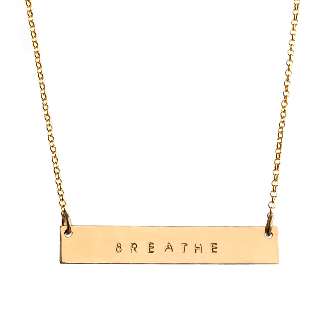 Gold Mantra Bar Necklace engraved with the word 'BREATHE,' hanging on a delicate gold chain, symbolizing mindfulness and simplicity. Handmade by Blooming Lotus Jewelry.