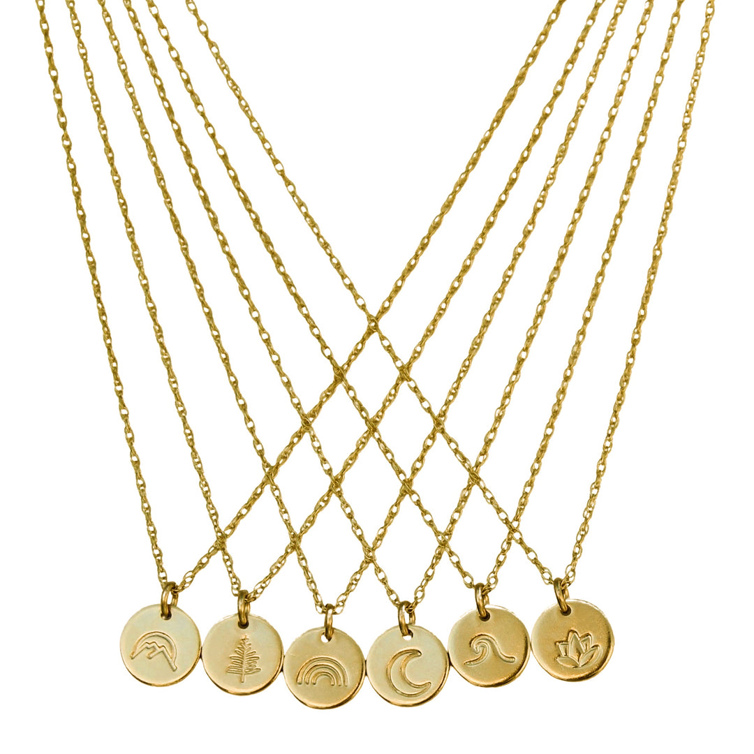 Collection of gold necklaces featuring tiny round disc  pendants, each hand-stamped with unique symbols including a mountain, tree, rainbow, crescent moon, wave, and lotus flower, arranged in an elegant crisscross display.